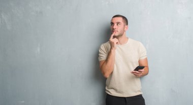 Gri grunge duvar manifatura bir ileti soru, çok karışık fikir hakkında smartphone ciddi bir yüz düşünme kullanarak üzerinde beyaz delikanlı