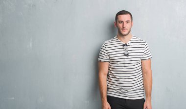 Beyaz delikanlı gri grunge duvarın yüzünde ciddi bir ifade ile üzerinden. Basit ve doğal kameraya bakıyor.