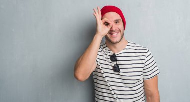 Mutlu yüz el parmaklarının arasından seyir göz üzerinde ok işaretiyle yapıyor gülümseyen ile yün şapkası gri grunge duvarın üzerinden beyaz delikanlı