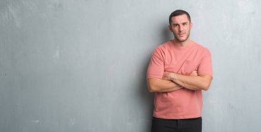 Gri grunge duvar şüpheci ve sinir, onaylamayan ifade yüz çapraz kolları olan genç beyaz adam. Negatif kişi.