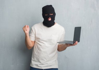 Duygu tezahürat Genç beyaz hacker adam gurur çığlık ve zafer ve başarı çok heyecanlı, kutluyor dizüstü kullanarak siber saldırı yapmak gri grunge duvarın üzerinden