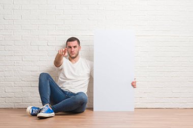 Şişe su ile kamera ve size, el işareti, pozitif ve kendinden emin bir jest ön parmakla holding beyaz tuğla duvar üzerine oturan genç beyaz adam