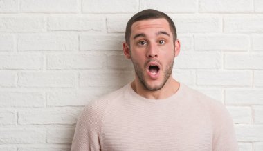 Genç beyaz adam ayakta beyaz tuğla duvarın bir sürpriz yüz, korkuyor ve heyecanlı korku ifadesi ile şok korkmuş üzerinden