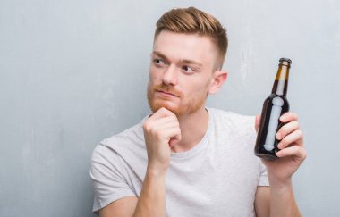Gri grunge duvar içki bira şişe ciddi bir yüz düşünme hakkında soru, çok karışık fikir genç Kızıl saçlı adam