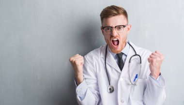 Genç redhead Doktor adam gri grunge Duvar ile öfke, çılgın ve yükseltilmiş eliyle diye bağıran rahatsız ve hayal kırıklığına uğramış öfke kavramı bağırarak