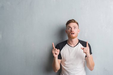 Genç Kızıl saçlı adam gri grunge duvarın üzerinden hayran ve yukarıya bakıp parmakları ile işaret şaşırttı ve silah kaldırdı.