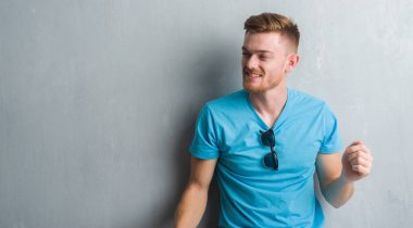 Genç Kızıl saçlı adam gri grunge duvar giyiyor rahat kıyafet uzak tarafına gülümseme ile yüzünde, doğal ifade arıyorum. Kendine güvenen gülüyor.