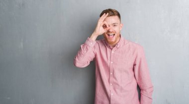 Sürpriz yüz, göz parmaklarının arasından seyir ile ok jest yapıyor genç redhead gri grunge duvar giyen üzerinde pembe gömlek şok. İmansız ifade.