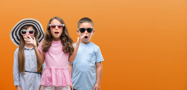Group of boy and girls kids over orange background scared in shock with a surprise face, afraid and excited with fear expression