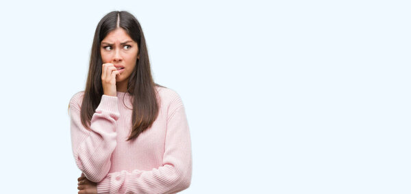 Young beautiful hispanic woman wearing a sweater looking stressed and nervous with hands on mouth biting nails. Anxiety problem.