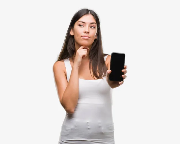 Jovem Bela Hispânica Mostrando Smartphone Rosto Sério Pensando Questão Ideia — Fotografia de Stock