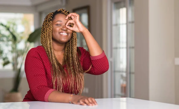 非洲裔美国妇女坐在家里与快乐的脸微笑做 签名用手在眼睛看通过手指 — 图库照片