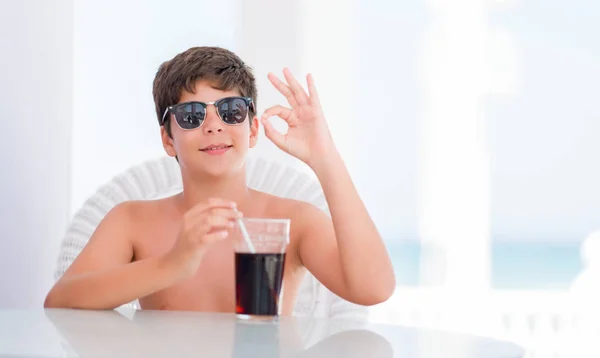 Young child on holidays drinking soda doing ok sign with fingers, excellent symbol
