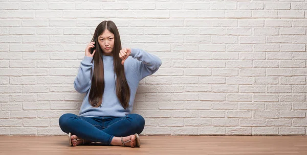 怒った顔 ダウン親指で嫌悪感を示すマイナス記号 拒絶反応の概念でレンガの壁に床に座っている若い中国女性 — ストック写真