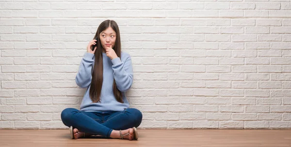 若い中国の女性に関する質問は 非常に混乱して考えレンガ壁深刻な顔を考えての上の床に座って — ストック写真