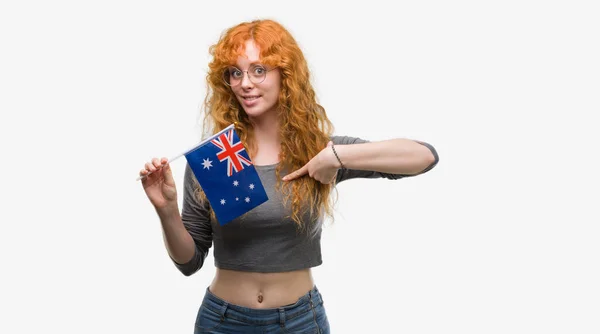 Joven Pelirroja Sosteniendo Bandera Australia Con Cara Sorpresa Señalando Dedo —  Fotos de Stock