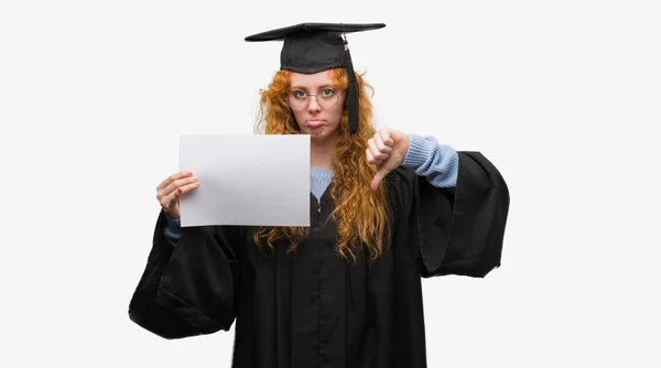 若い赤毛の女性が怒っている顔 ダウン親指で嫌悪感を示すマイナス記号 拒絶反応の概念との程度を保持している大学院の制服を着て — ストック写真