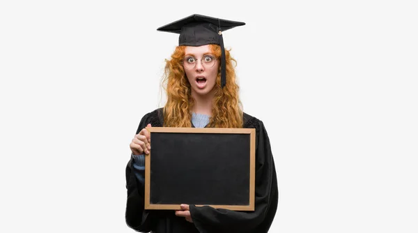 Young Redhead Student Woman Wearing Graduated Uniform Holding Blackboard Scared — Stock Photo, Image