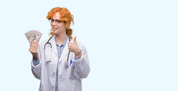 Joven Pelirroja Médico Mujer Sosteniendo Dólares Feliz Con Gran Sonrisa —  Fotos de Stock