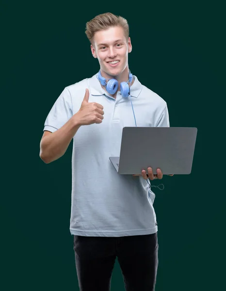 笑顔の サイン 優秀な兆候を親指をやって幸せなノート パソコンを使用して若いハンサムな金髪男 — ストック写真