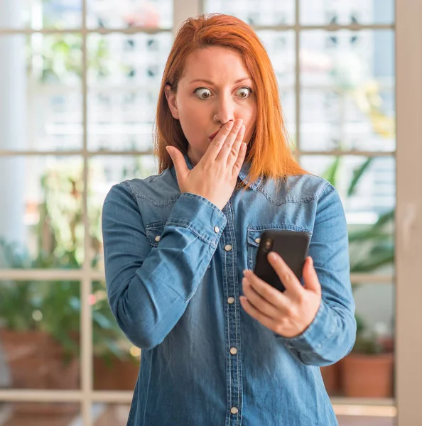 Rusovláska Žena Pomocí Smartphone Doma Kryt Ústa Rukou Šoku Studem — Stock fotografie