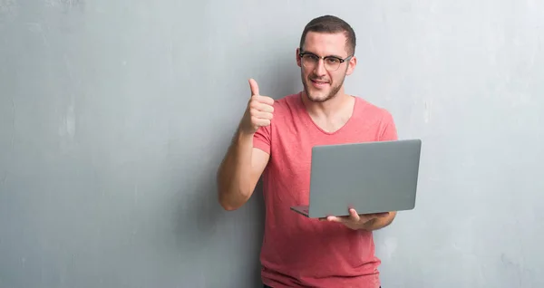 Young Caucasian Man Grey Grunge Wall Using Computer Laptop Happy — Stock Photo, Image