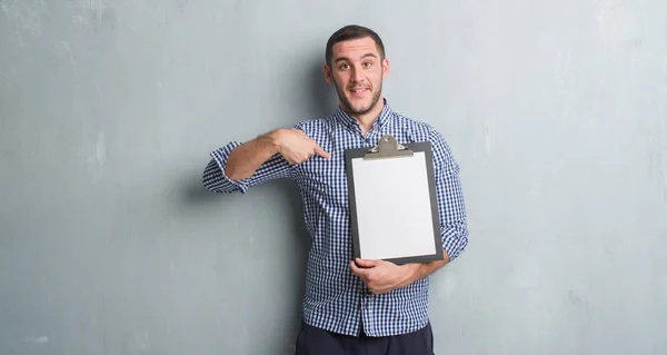 Joven Caucásico Hombre Sobre Gris Grunge Pared Celebración Portapapeles Con —  Fotos de Stock