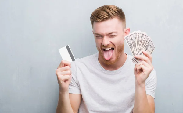 Young Redhead Man Holding Dollars Credit Card Sticking Tongue Out — Stock Photo, Image