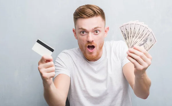 Young Redhead Man Holding Dollars Credit Card Scared Shock Surprise — Stock Photo, Image