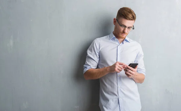 Young Redhead Man Grey Grunge Wall Sending Message Using Smartphone — Stock Photo, Image