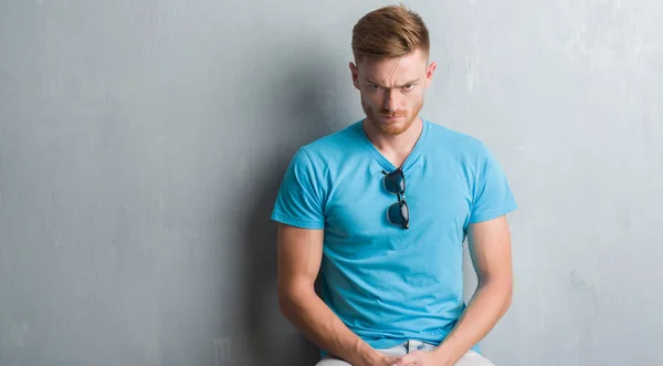 Young redhead man over grey grunge wall wearing casual outfit skeptic and nervous, frowning upset because of problem. Negative person.