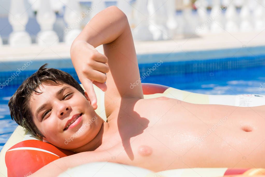 Young child on pad on holidays at the swimming pool by the beach very happy pointing with hand and finger