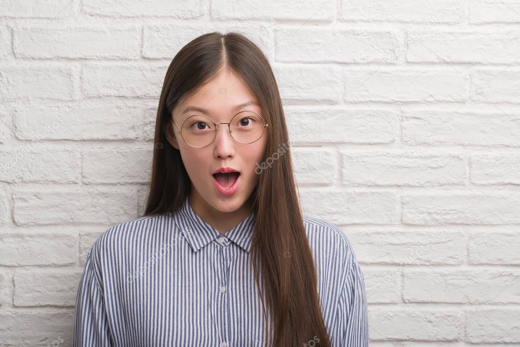 Young Chinese business woman over brick wall scared in shock with a surprise face, afraid and excited with fear expression