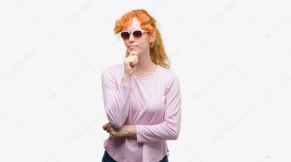Young redhead woman wearing sunglasses serious face thinking about question, very confused idea