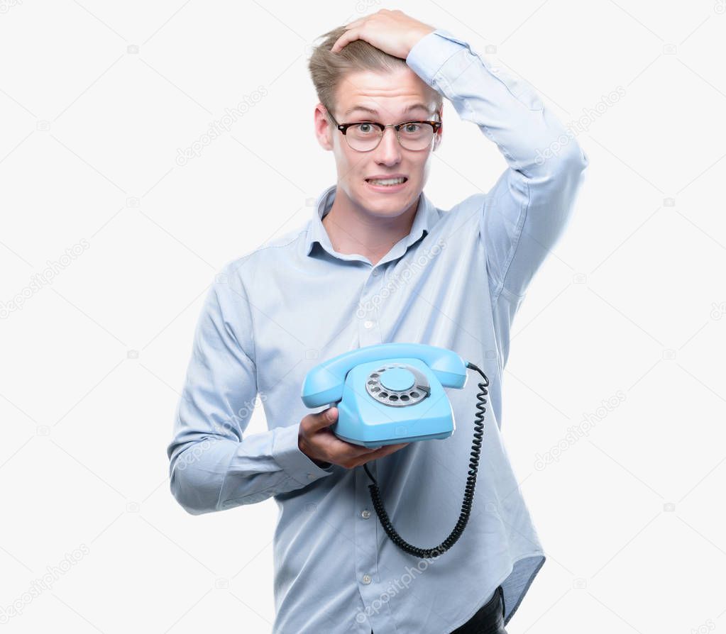 Young handsome blond man holding vintage telephone stressed with hand on head, shocked with shame and surprise face, angry and frustrated. Fear and upset for mistake.