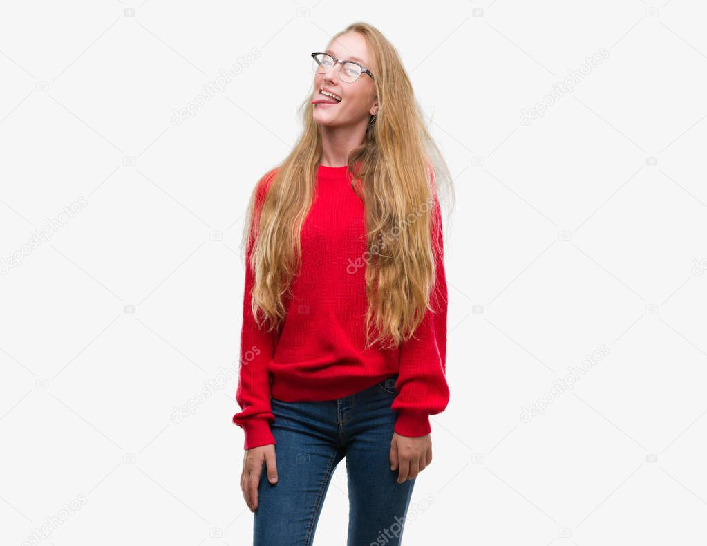 Blonde teenager woman wearing red sweater sticking tongue out happy with funny expression. Emotion concept.