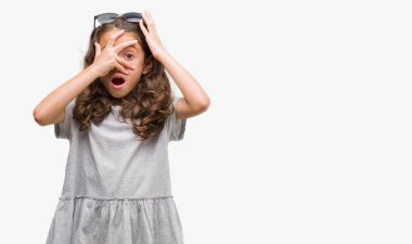 Mahcup ifadeyle parmaklarımın arasından seyir esmer İspanyol kız yüz ve gözler el ile kapsayan şok bakmak güneş gözlüğü takıyor.