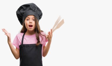 Esmer Latin kız kocaman bir gülümseme ile çığlık zaferini kutluyor ve ellerini kaldırdı aşçı üniforma çok mutlu ve heyecanlı, kazanan ifade giyiyor