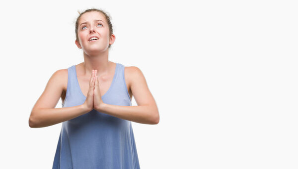 Young blonde woman begging and praying with hands together with hope expression on face very emotional and worried. Asking for forgiveness. Religion concept.