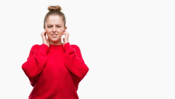 パンと赤いセーター騒々しい音楽のノイズの腹が立つ式の指を使って耳をカバーを身に着けている若いブロンドの女性 聴覚障害者の概念 — ストック写真