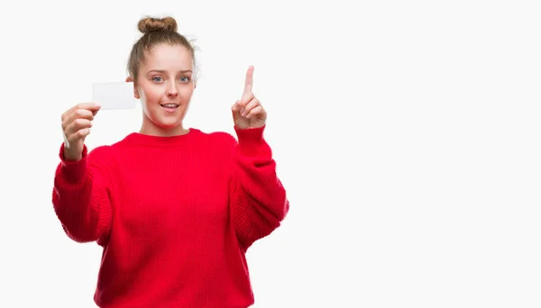 幸せそうな顔 ナンバーワンのアイデアや質問ポインティング指で驚く広告カードを保持している若いブロンドの女性 — ストック写真