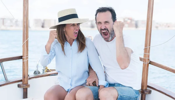 Middle age couple traveling on sailboat annoyed and frustrated shouting with anger, crazy and yelling with raised hand, anger concept