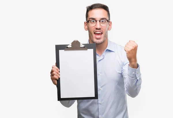 Joven Hombre Negocios Guapo Mostrando Portapapeles Gritando Orgulloso Celebrando Victoria — Foto de Stock