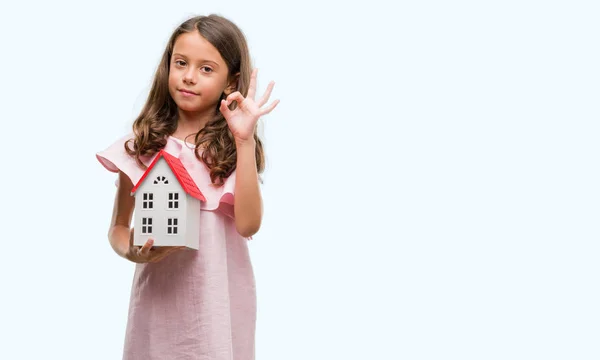 優秀なシンボルの指で サインをして小さな家を保持しているヒスパニックのブルネットの少女 — ストック写真