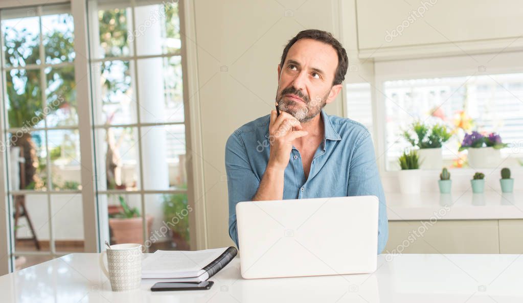 Middle age man using laptop at home serious face thinking about question, very confused idea
