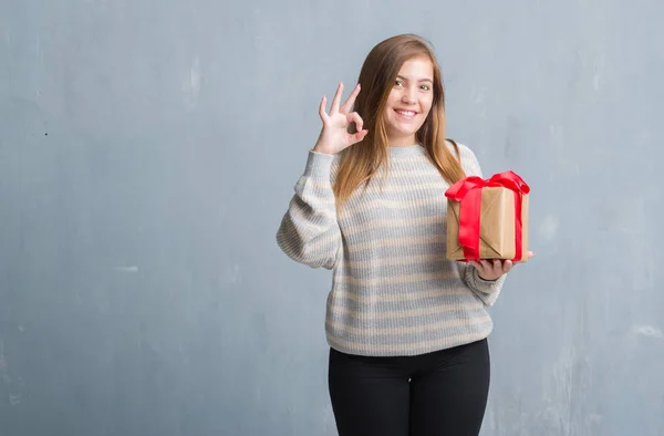 Young Adult Woman Grey Grunge Wall Holding Present Doing Sign — Stock Photo, Image