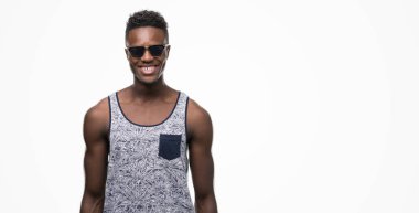 Genç Afro-Amerikan adam ayakta ve diş gösterilen kendine güvenen bir gülümsemeyle gülümseyerek mutlu bir yüz ile