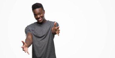 Sarılmak için kollarını açarak gülümseyerek kameraya bakarak gri t-shirt giyen genç Afro-Amerikan adam. Neşeli ifade kucaklayan mutluluk.