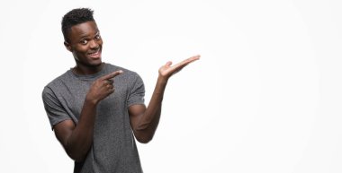 Hayret ve el ile sunulması ve parmak ile işaret ederken kameraya gülümseyen gri t-shirt giyen genç Afro-Amerikan adam.