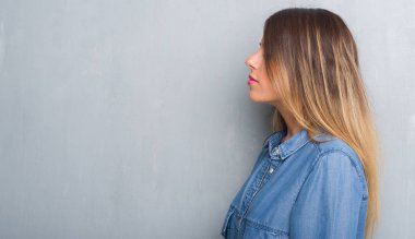 Grunge gri duvar tarafına, seyir kot kıyafeti giymiş genç yetişkin kadın dinlenmek doğal yüz emin gülümseme ile pozuyla profili.